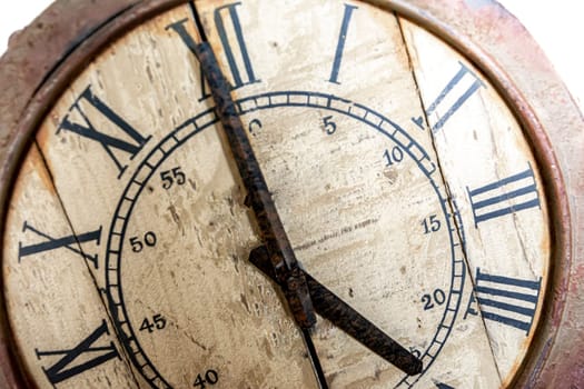 Old vintage and retro analogue clock displaying five o' clock. Worn-out and grunge style with wooden background.