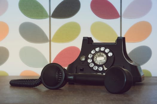 Old retro and vintage phone off the hook against colorful wallpaper. Muted processing.