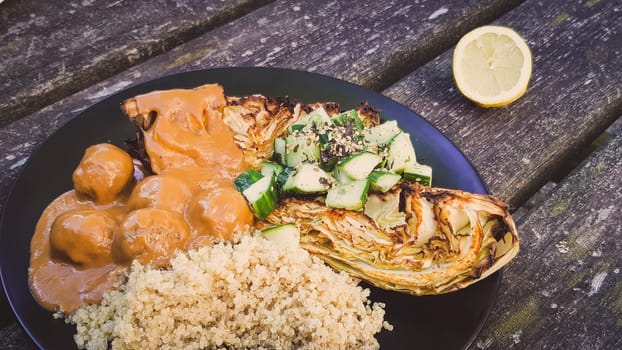 Vegan dish with oven baked cabbage, cucumber, vegan meatballs in Peanut Sauce and quinoa, lemon on the side on weathered wooden table