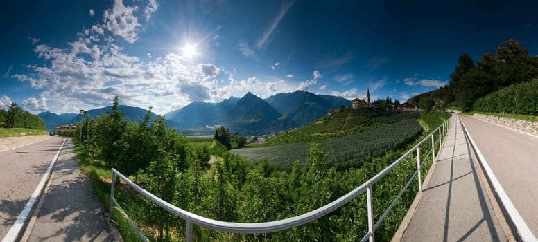 Wide-angle panorama view of the road from Schenna to Sankt Georgen with a view over the apple orchards in the light of the sun in South Tyrol in summer 2013. Panoramic composed from multiple images.