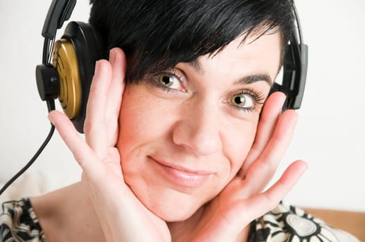 Head portrait of a young black-haired woman with headphones and hands on cheeks against white background.