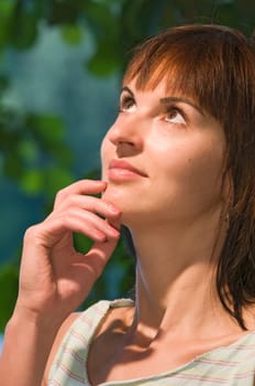 Partial head portrait of a young woman looking up, thoughtfully holding her right hand to her chin.