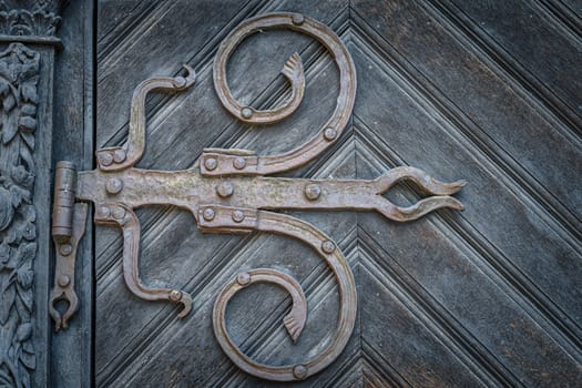 Closeup on vintage iron hinges in baroque style on wooden door with frame ornaments. Cathedral in Szczecin, Poland