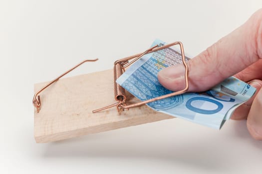 Thumb caught in a mousetrap when reaching for a 20 euro note on a white background.