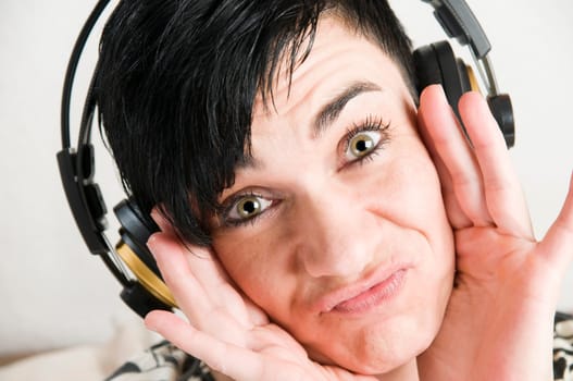 Head portrait of a young black-haired woman with headphones and hands on cheeks against white background.