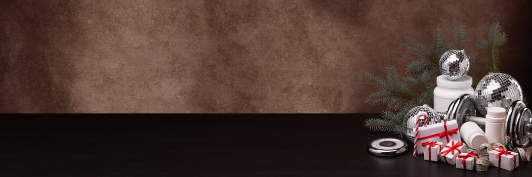 Sports nutrition (supplements), sports equipment, fir branch,  gift boxes, Christmas ornaments on dark brown background with copy space. Fitness, sport, healthy lifestyle concept. New Year. Christmas.