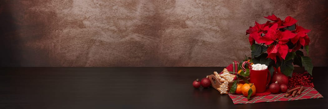Red Poinsettia flowers, tray with ginger cookies and mandarines, mug with hot cocoa and marshmallows. fir ornaments on brown background with copy space. Winter holidays. New Year, Christmas treat.