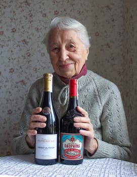 Kyiv, Ukraine - November 15, 2020: The old woman with bottles of red dry wine from Cabernet, Garnacha and syrah from Cotes du Rhone, France, 2018