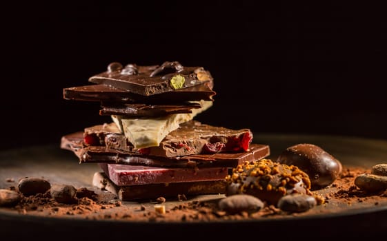 Stack of assorted chocolate with cocoa and cocoa beans on black background