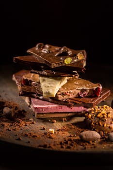 Stack of assorted chocolate with cocoa and cocoa beans on black background