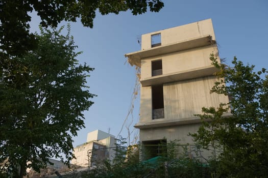 Ruined large concrete building undergoing demolition. Wider angle with industrial concrete buildings in the background. Morning sunshine, gentle sky