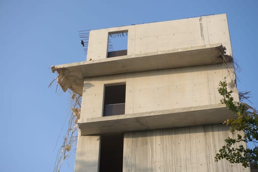 Plain blue background behind the top three floors of an empty concrete building. Partly wrecked and demolished as steel supports hang out with rubble