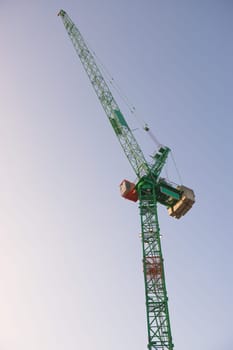Top portion a tall tower crane at sunrise with a bright sky background. Modern construction machinery with fresh green and orange colors. metal frame.