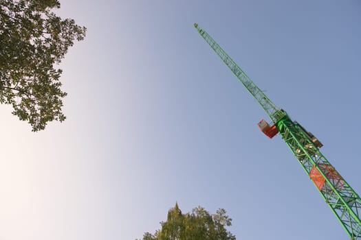 Smooth early morning sky background behind the leaves of tree tops and the leading jib of a large tower crane. Abstract with plenty of copy space.