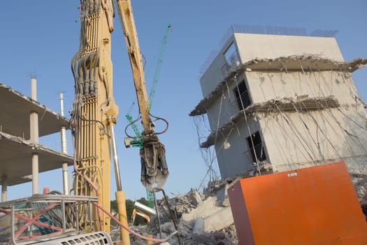 Concrete rubble and hanging steel cables on this demolition site, Large high reach demolition excavator in the foreground, with tower crane behind