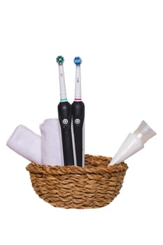 Two electrical tooth brushes, an oral care product or toothpaste and towels in a basket isolated on a white background. Dental and healthcare concept. Copy space.