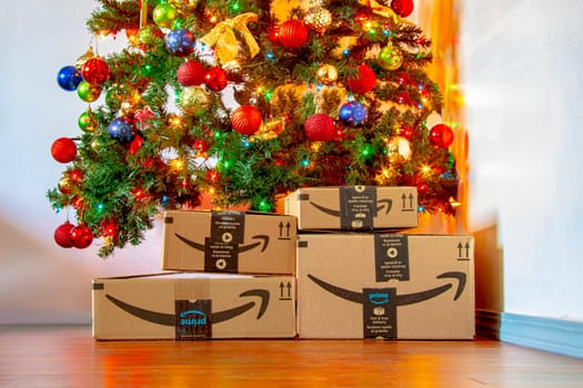 Calgary, Alberta, Canada. Nov. 16, 2020. Amazon boxes under a Christmas tree with ornaments and lights on. Concept: Shopping during the holidays.