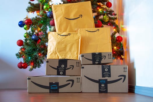 Calgary, Alberta, Canada. Nov. 16, 2020. Amazon boxes and envelopes under a Christmas tree with ornaments and lights on. Concept: Delivering packages during the holiday season.