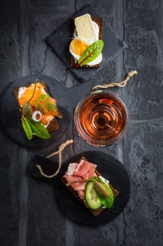 Variation of healthy open sandwiches on Pumpernickel bread with vegetables, salmon, ham, herbs, soft cheese and glass of red wine