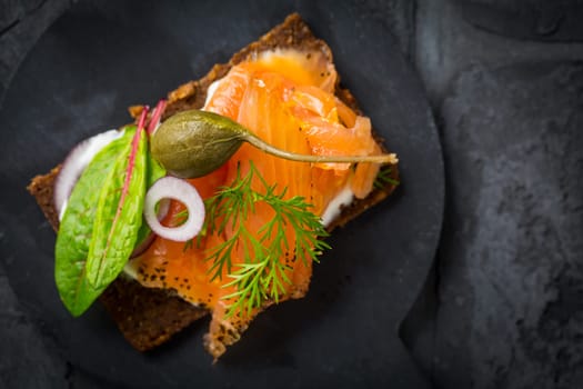 Salmon open sandwich on Pumpernickel bread with vegetables, herbs and soft cheese