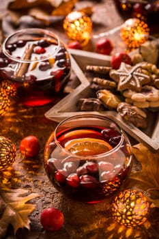 Mulled wine with orange, cranberries, cinnamon, anise with cookies, autumn leaves and Christmas lights