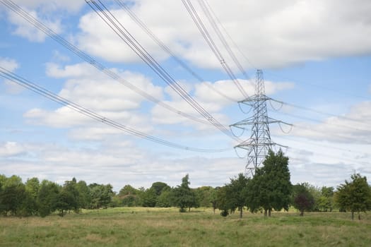 Landscape image of large metal electricity pylon and overhead power lines in a rural countryside setting. Summer season and green trees on the land