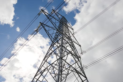 Low angle image of an electrical transmission lattice tower. High voltage power lines silhouetted against the summertime sky. Spacers hang from tower