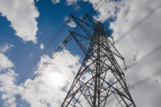 Environmental contrasts, big dark metal electrical pylon against a natural cloudy blue sky. Copy space to left hand side, bright sunlight