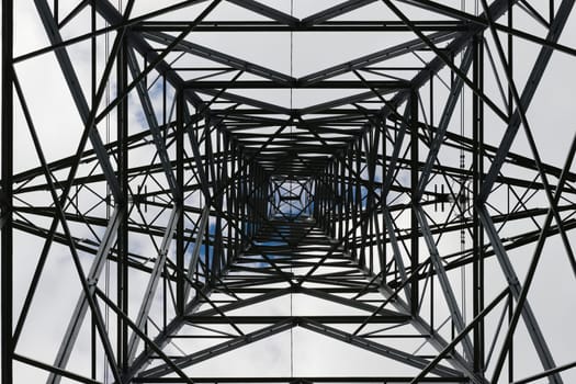 Dark abstract image of the inside of an electrical pylon. Interior skyward view, looking up, lattice structure creates an industrial themed pattern.