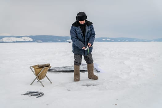 Baikal lake, Siberia, Russia - March 05, 2020 : Winter ice fishing. A fisherman is fishing on spinings near tents and cars on Lake Baikal on a March day. Baikal lake, Siberia, Russia-96