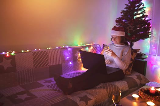 Happy woman making a toast on video call celebrating Christmas with glass of wine, online during coronavirus outbreak. Celebrating Christmas in lockdown.