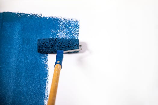 Paintign the wall in blue with roller brush.