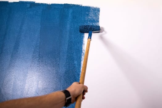 Paintign the wall in blue with roller brush.
