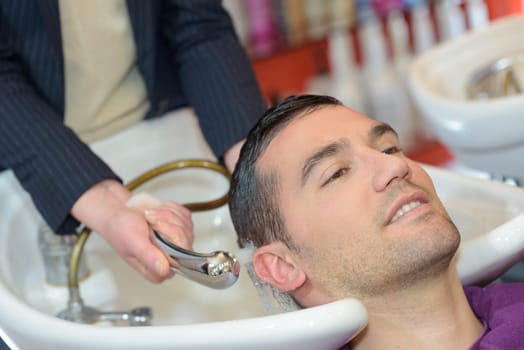 female hairdresser washing handsome clients hair