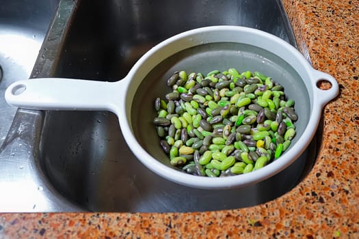 Fresh green beans being drained in a colander over the sink.