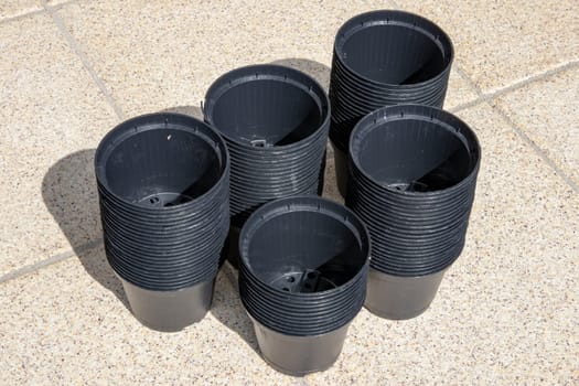 Closeup of empty black plastic plant pots stacked on the terrace on a sunny day. Equipment of the gardener for planting out seedlings.