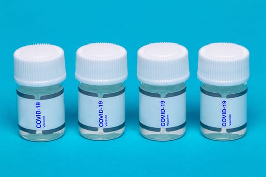 Treatment coronavirus. Close-up of four plastic containers with transparent liquid and the inscription Covid-19 vaccine on blue background. Copy space.