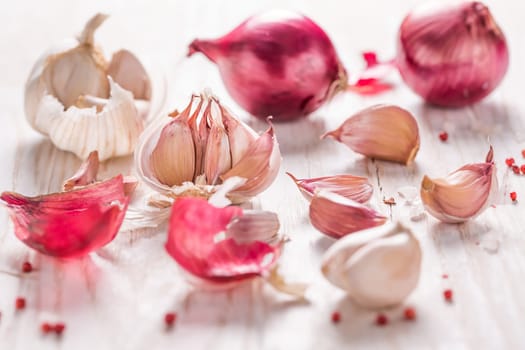 Garlic bulb, garlic cloves and red onions on white wooden background