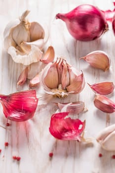 Garlic bulb, garlic cloves and red onions on white wooden background