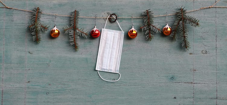 Corona and Christmas. A protective mask hangs next to Christmas tree balls and fir branches