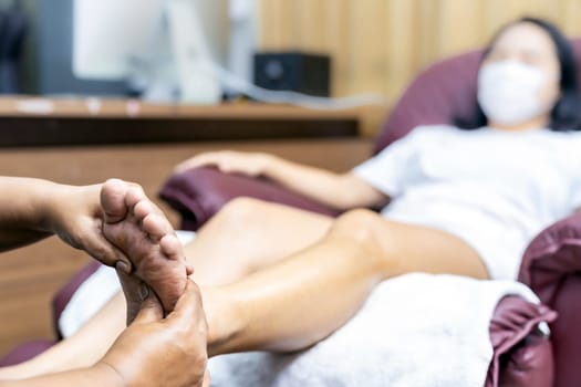 Close up asian woman do foot massage at home with face mask while city lockdown for social distance due to coronavirus pandemic. Massage is one of service business that shutdown while city lockdown.