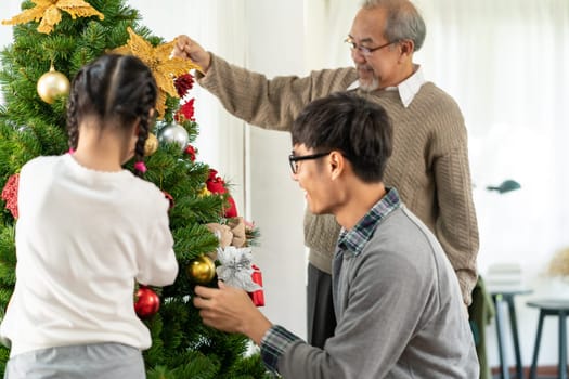 Multigenerational asian Family decorating a Christmas tree. Mom Dad daughter girl and grandfather decorate the Christmas tree prepare for season greeting of Merry Christmas and Happy Holidays.
