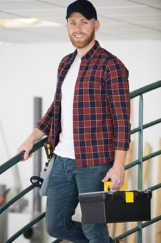 young smiling tradesman holding toolbox while walking down stairs