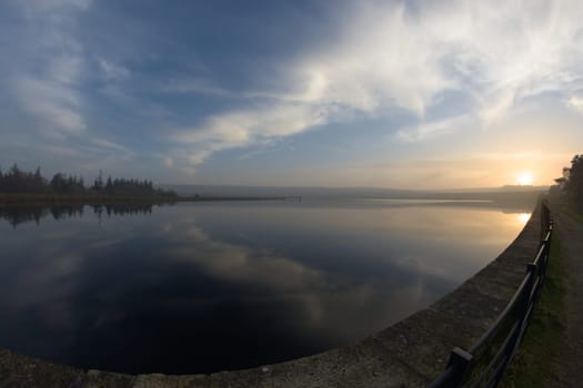 Middle reservoir at redmires reservoirs near sheffield, flat calm at sunset. Fish eye perspective as the water reflects the sunset sky of wispy clouds