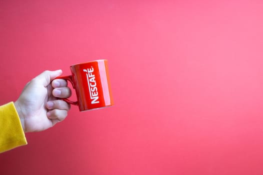 Kuala Lumpur, Malaysia - November 12, 2020 : Hand holding Nescafe Mug on red background