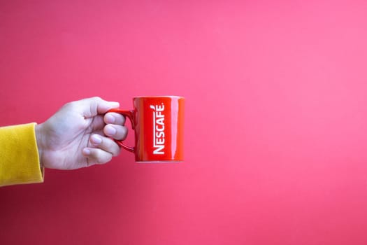 Kuala Lumpur, Malaysia - November 12, 2020 : Hand holding Nescafe Mug on red background