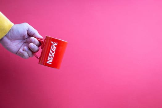 Kuala Lumpur, Malaysia - November 12, 2020 : Hand holding Nescafe Mug on red background
