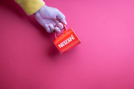 Kuala Lumpur, Malaysia - November 12, 2020 : Hand holding Nescafe Mug on red background