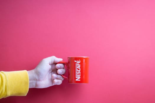 Kuala Lumpur, Malaysia - November 12, 2020 : Hand holding Nescafe Mug on red background