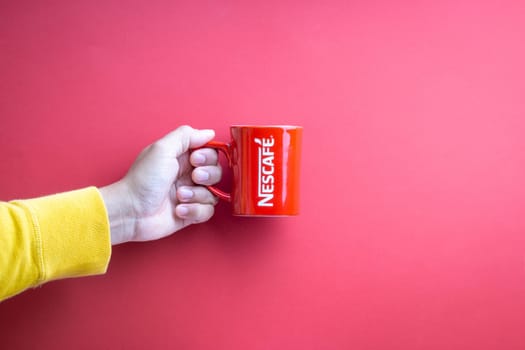 Kuala Lumpur, Malaysia - November 12, 2020 : Hand holding Nescafe Mug on red background